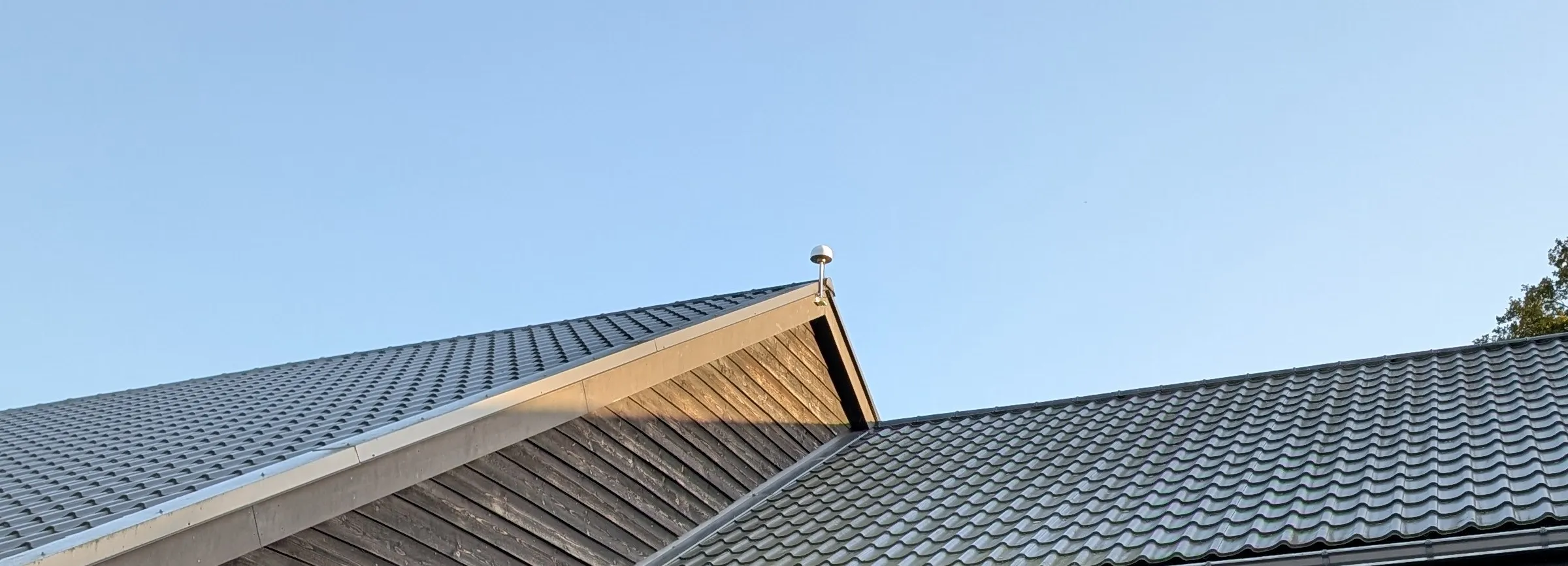 Witte GNSS-referentiestation-antenne op de nok van een schuur, tegen blauwe lucht