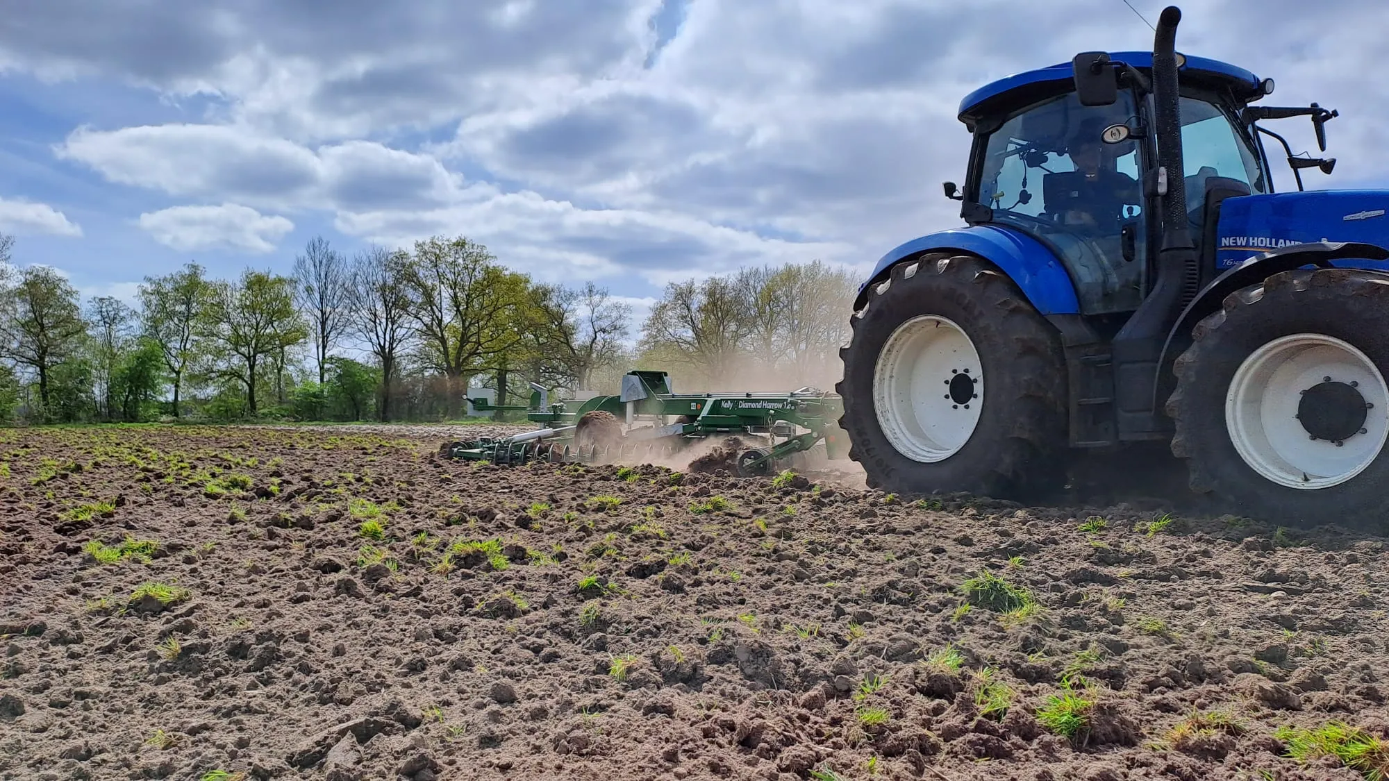 New Holland-trekker met kettingeg (Kelly) bewerkt een akker, met opstuivend stof